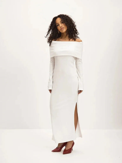 Model wearing the Sculpted Grace Maxi Dress, a white off-shoulder dress with a side slit, perfect for weddings and formal events.