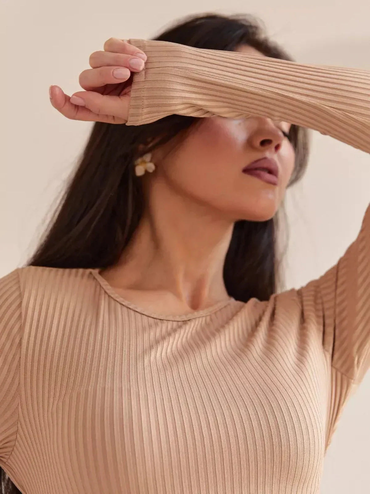 Close-up of a model showcasing a ribbed long sleeve dress in a soft beige tone, emphasizing elegance and comfort.