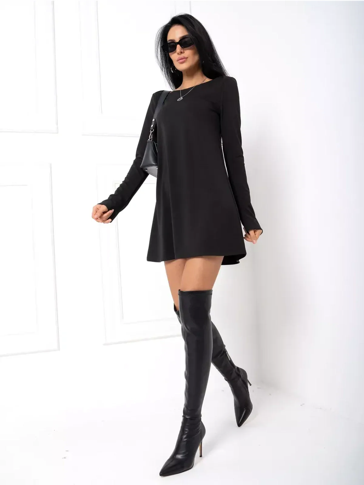 Stylish woman in a black mini dress with long sleeves and thigh-high boots, perfect for cocktail or casual occasions.