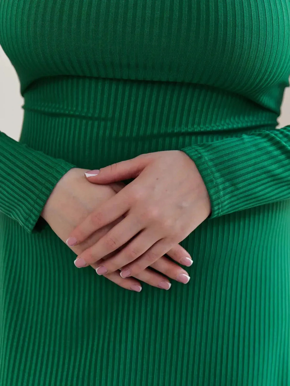 Close-up of hands clasped in front of a model wearing a ribbed green Luxe Sculpt Midi Dress, showcasing its elegant design.
