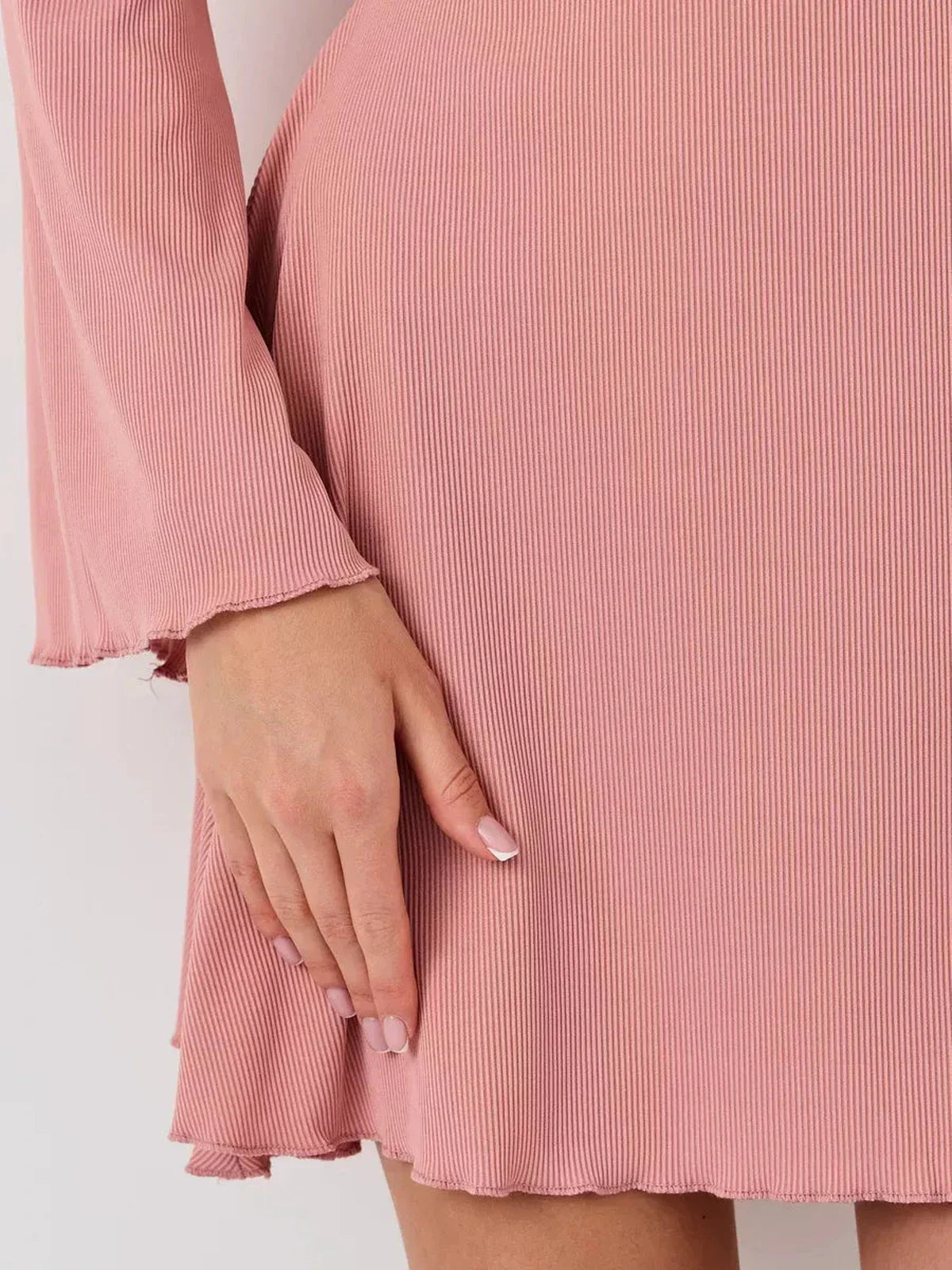Close-up of a hand on the hem of the Blush Aura pink mini dress, showcasing its soft, stretchy fabric and flared sleeves.