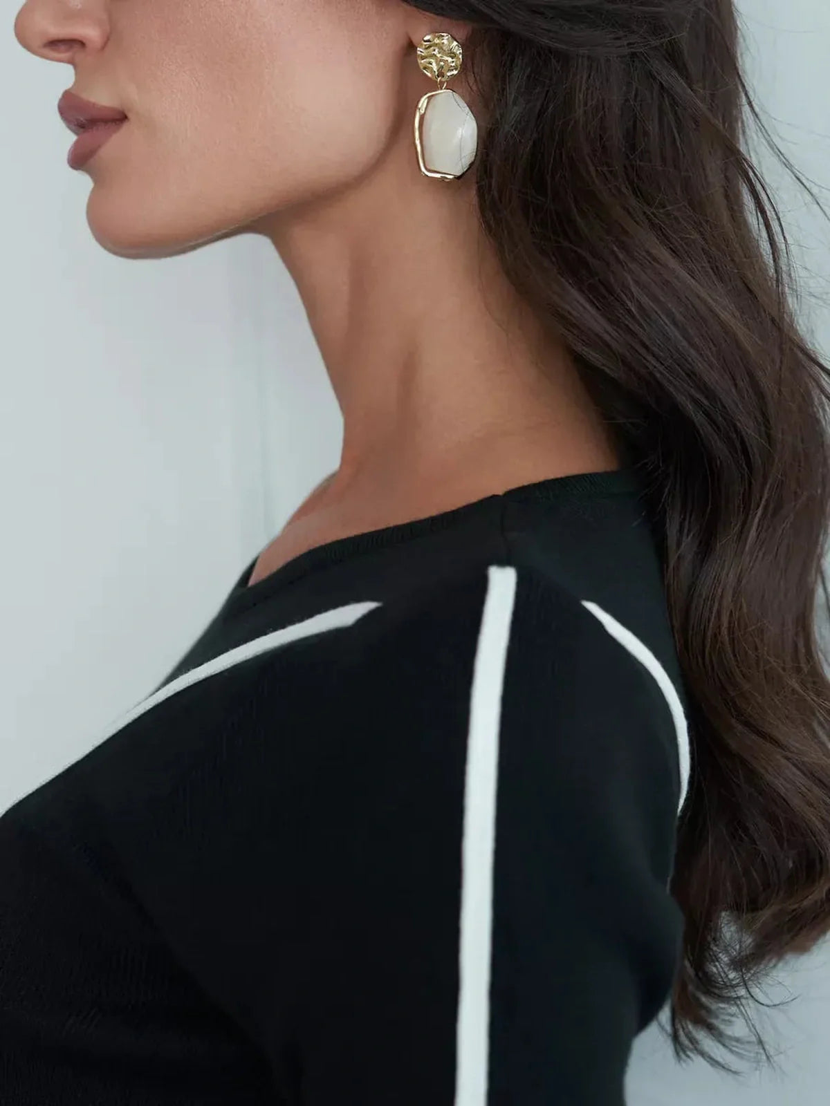 Close-up of a woman wearing elegant gold and white earrings, showcasing a sophisticated style with black dress detailing.