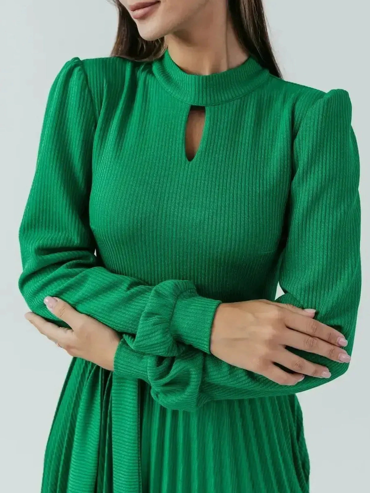 Close-up of a woman in a green ribbed knit midi dress with elegant pleats and a modern stand collar.