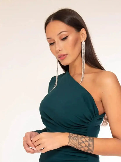 Elegant woman in a one-shoulder emerald green maxi dress, showcasing a sultry side slit and statement earrings.