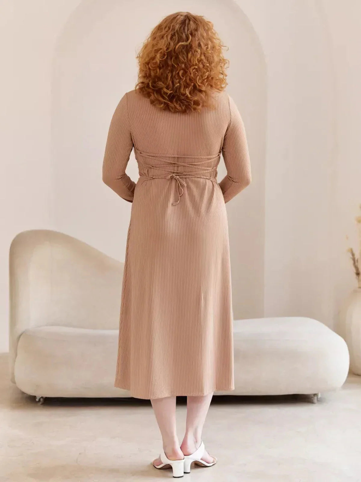 Rear view of a woman in a nude Laced Elegance Midi Dress, showcasing its lace-up waist design and long sleeves.