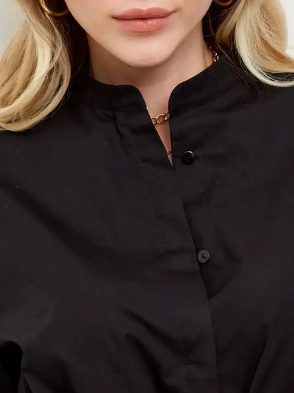 Close-up of a woman wearing a black minimalist dress with a stand collar and button details, showcasing elegance.