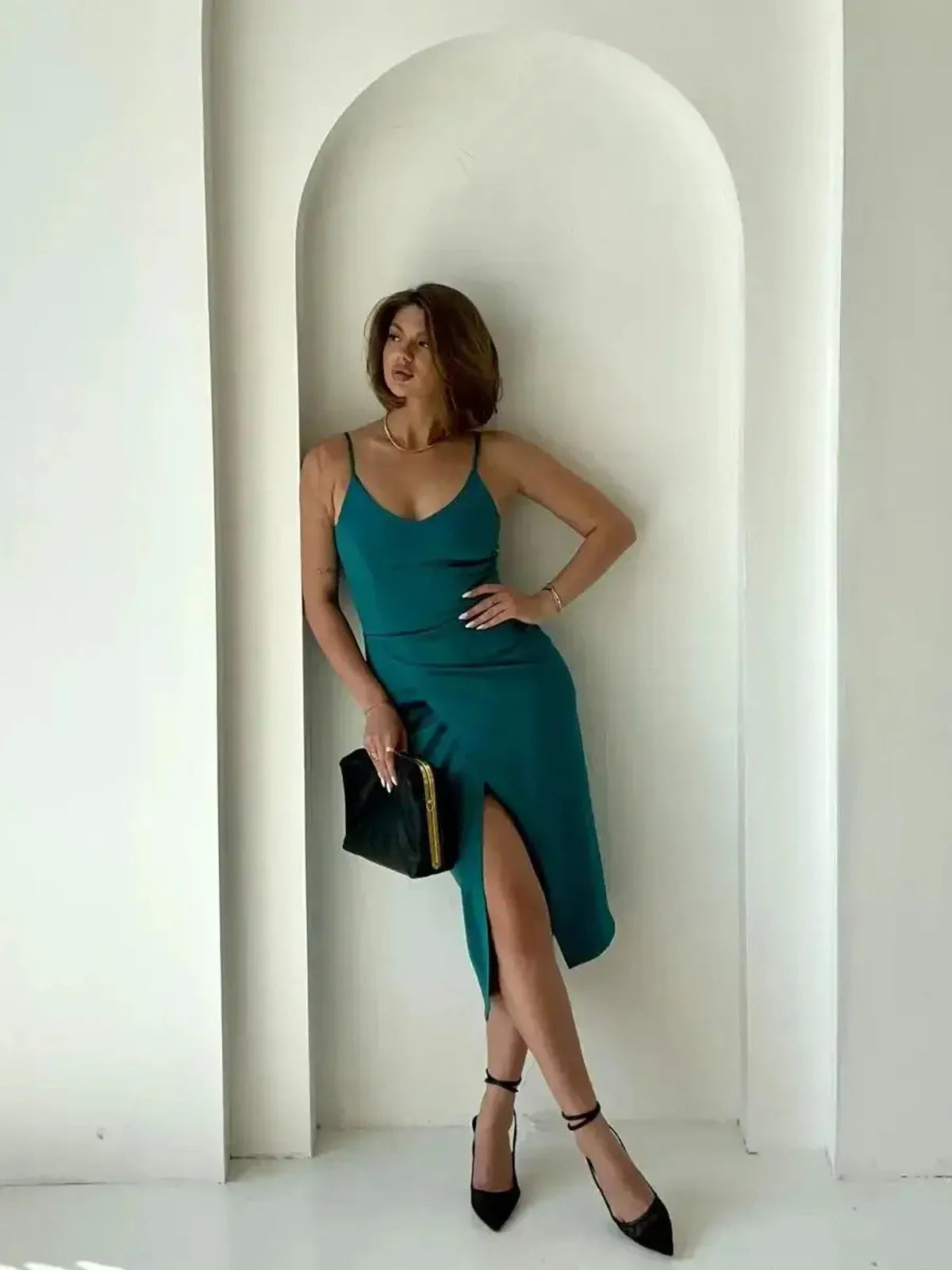 Model showcasing the Lustre Midi Dress in emerald green, featuring a sleek design and thigh-high slit against a minimalist backdrop.
