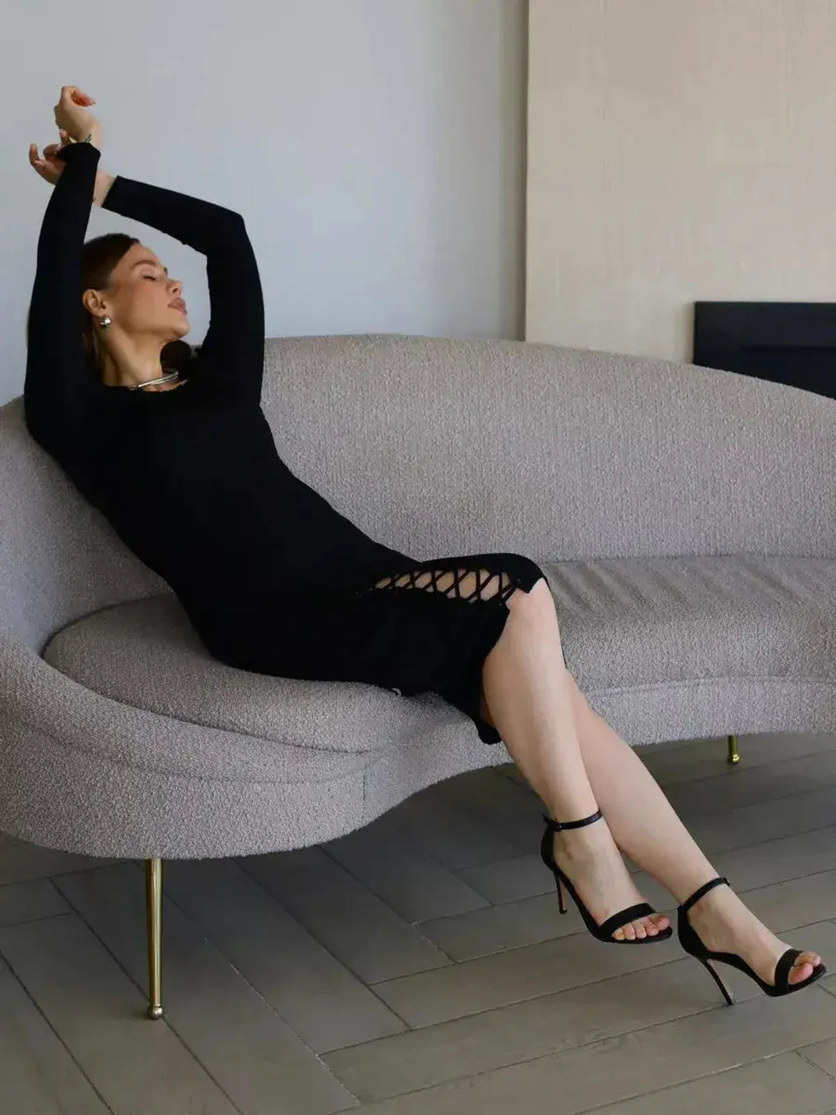 Woman in a fitted black midi dress with lace-up details, lounging stylishly on a modern sofa, perfect for chic occasions.