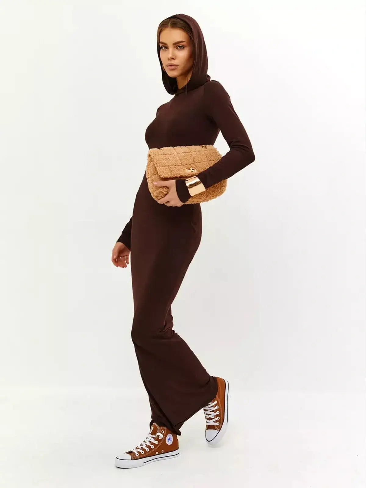 Model wearing a hooded Sculpt Maxi Dress in rich chocolate, paired with sneakers and a stylish bag, showcasing casual elegance.