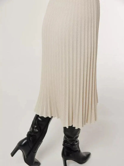 Ivory pleated midi dress with tailored waist, paired with stylish black high-heeled boots.