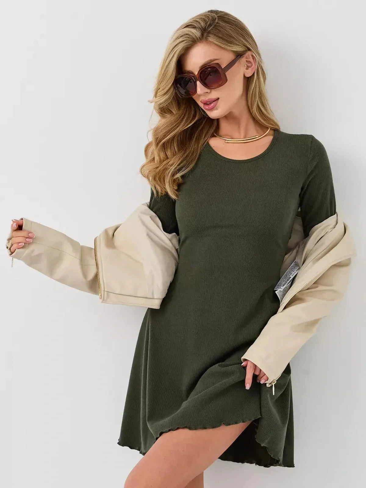 Stylish woman in an olive green mini dress with flared sleeves, paired with a beige jacket and sunglasses.