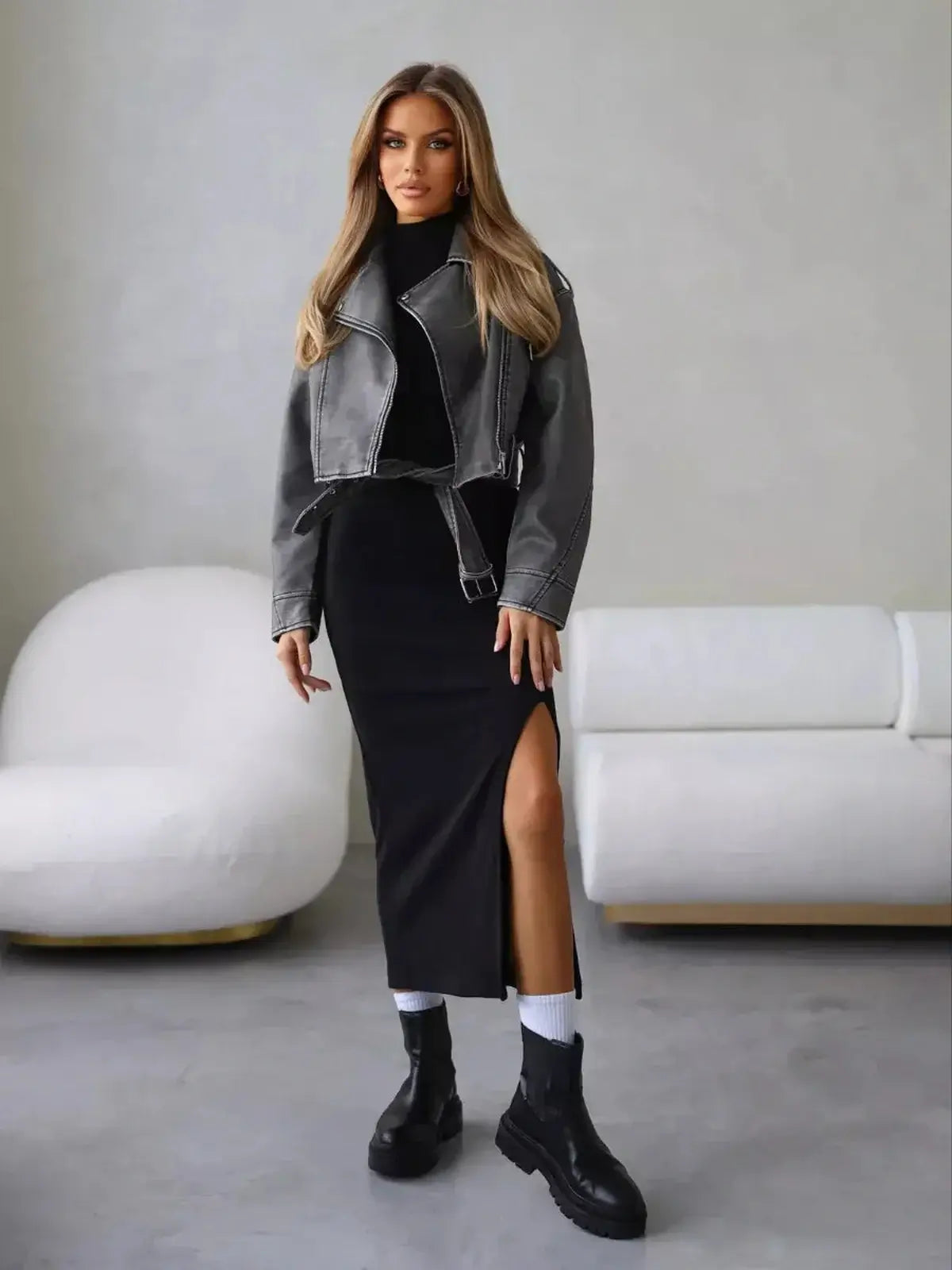 Woman in a sleek black midi dress with a high slit, styled with a grey leather jacket and black boots, ideal for casual chic looks.