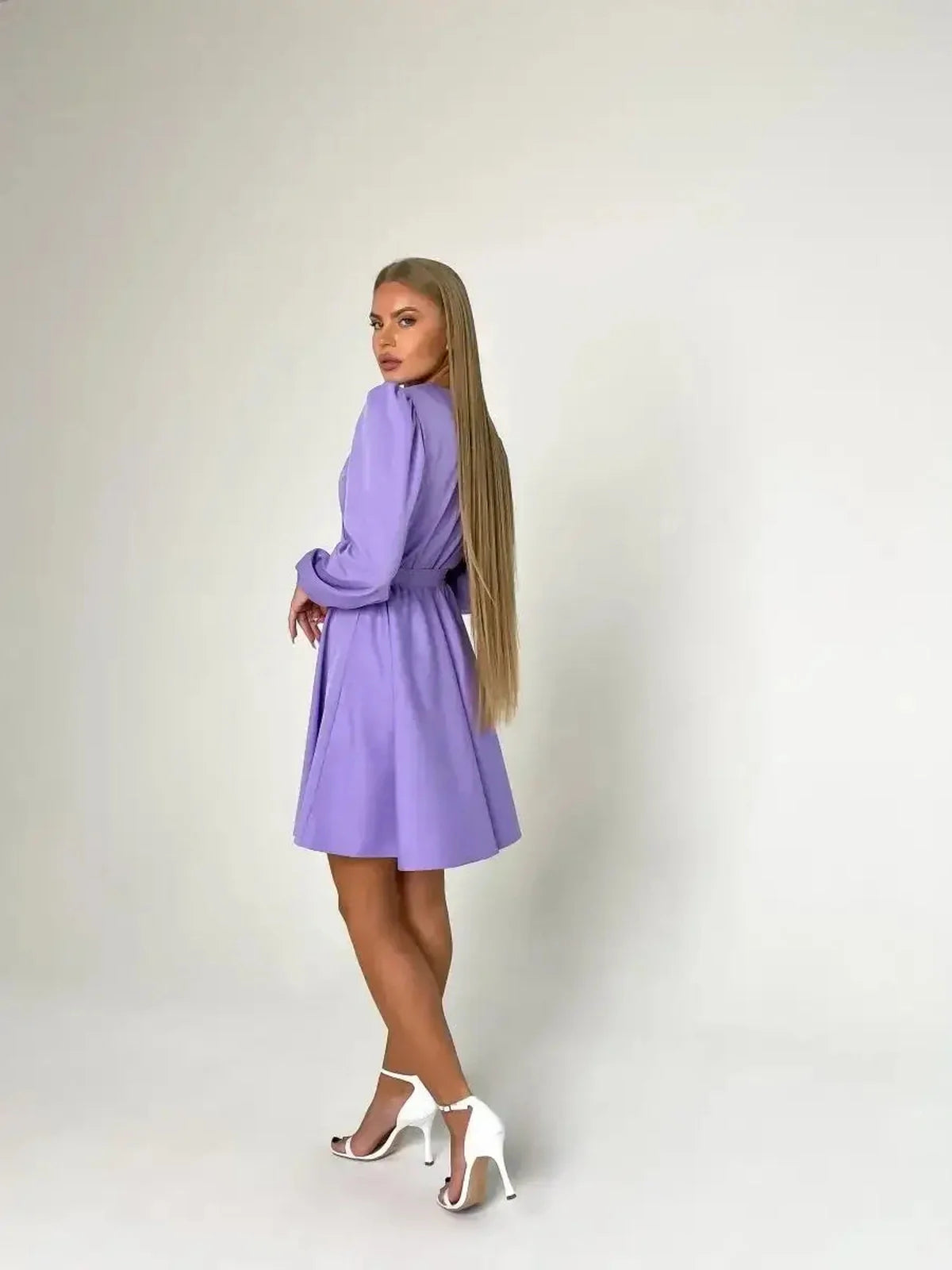 Model showcases the Lilac Charm mini dress in lavender, featuring a cinched waist and elegant long sleeves, ideal for weddings.