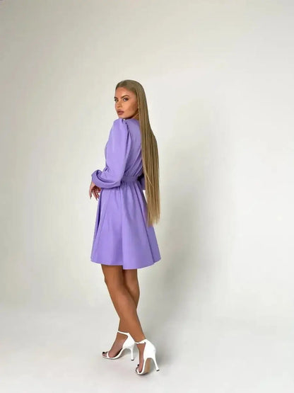 Model showcases the Lilac Charm mini dress in lavender, featuring a cinched waist and elegant long sleeves, ideal for weddings.