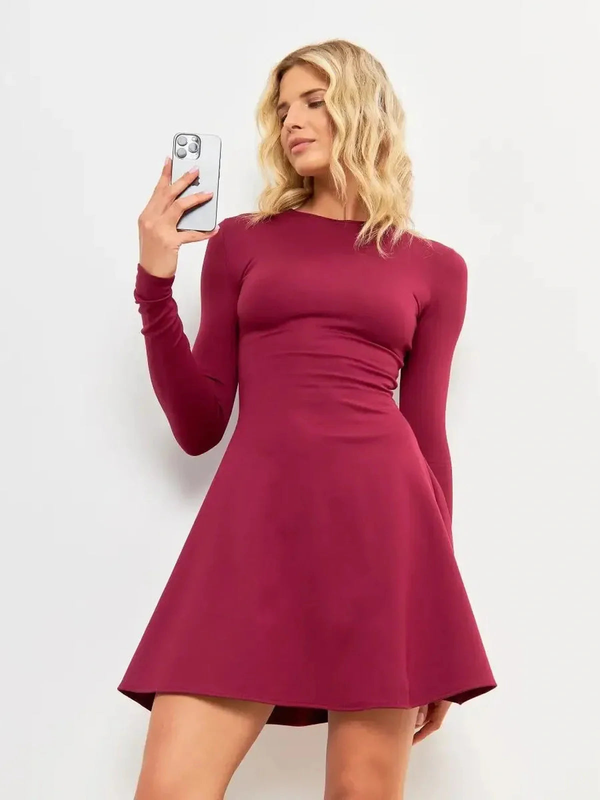 Elegant woman wearing the Wine Flare Mini dress in burgundy, showcasing a flattering silhouette and long sleeves.