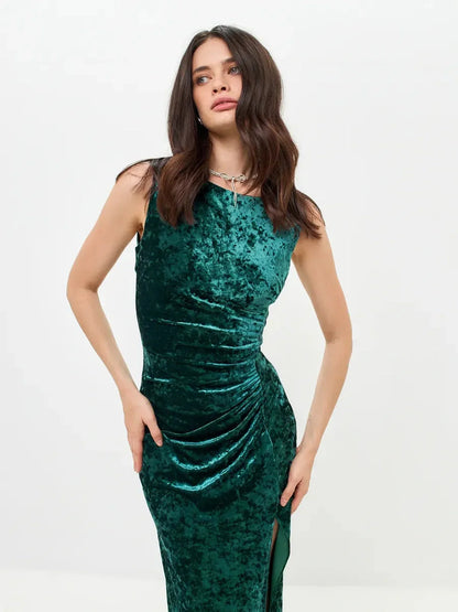 Woman modeling the Velvet Aura Maxi Dress in green, featuring sleek fit, ruching, and a high slit for elegant occasions.