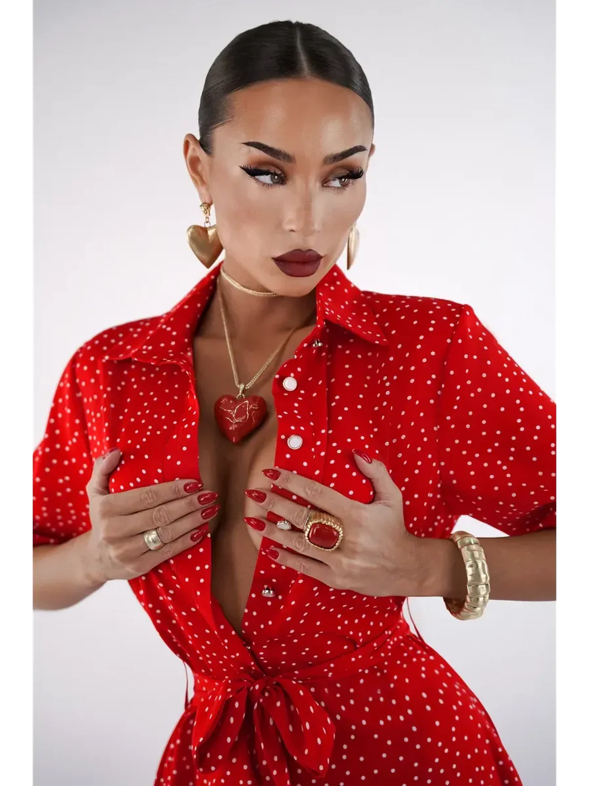 Woman wearing a vibrant red polka dot midi dress with a V-neckline and cinched waist, showcasing bold jewelry.
