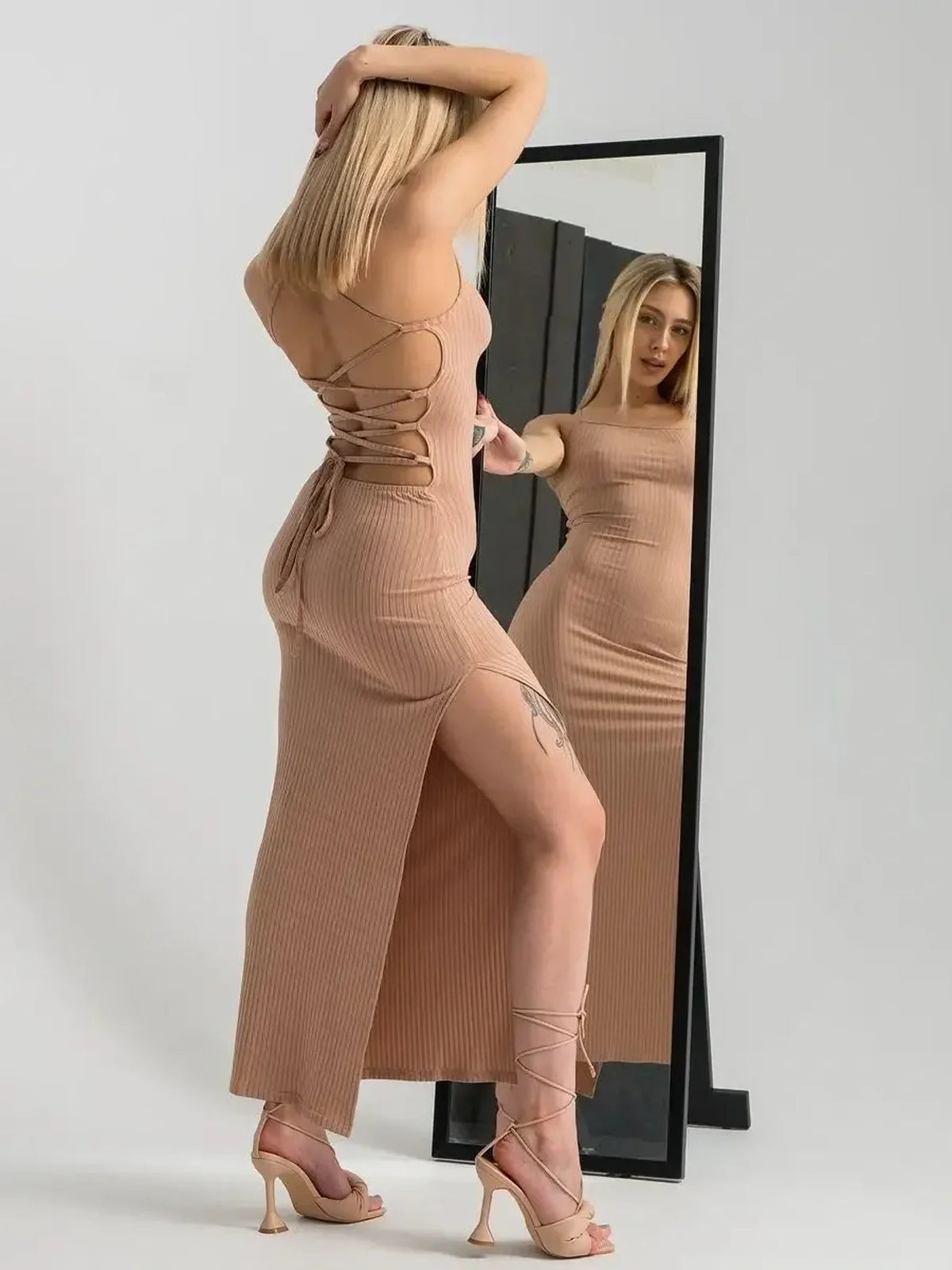 Nude lace midi dress featuring a sculpting ribbed fit, corset back, and thigh-high slit, styled with heels and mirror reflection.