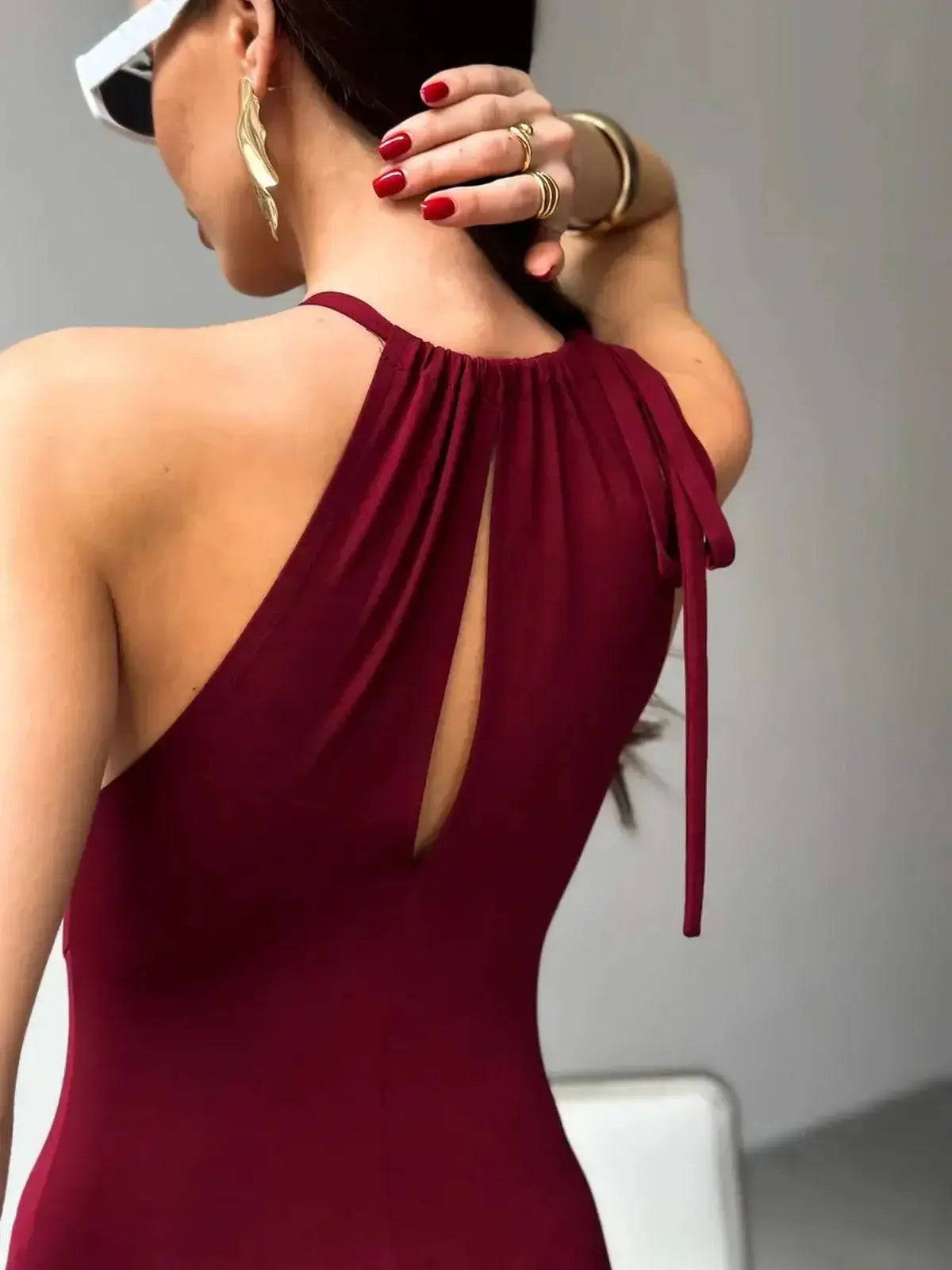 Back view of a woman in a burgundy maxi dress with draped halter neckline and keyhole detail, showcasing elegant style.