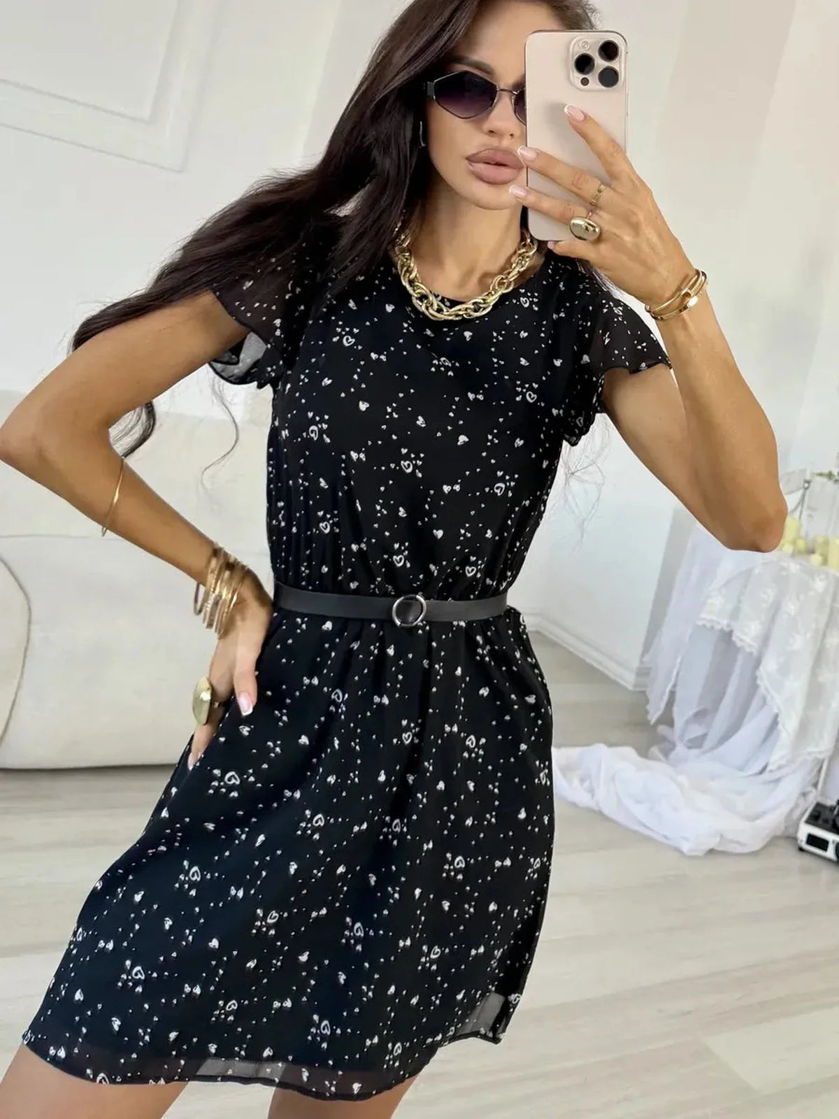 Stylish woman in a black chiffon mini dress with white dots and flutter sleeves, accessorized with sunglasses and a belt.