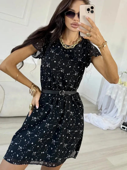 Stylish woman in a black chiffon mini dress with white dots and flutter sleeves, accessorized with sunglasses and a belt.