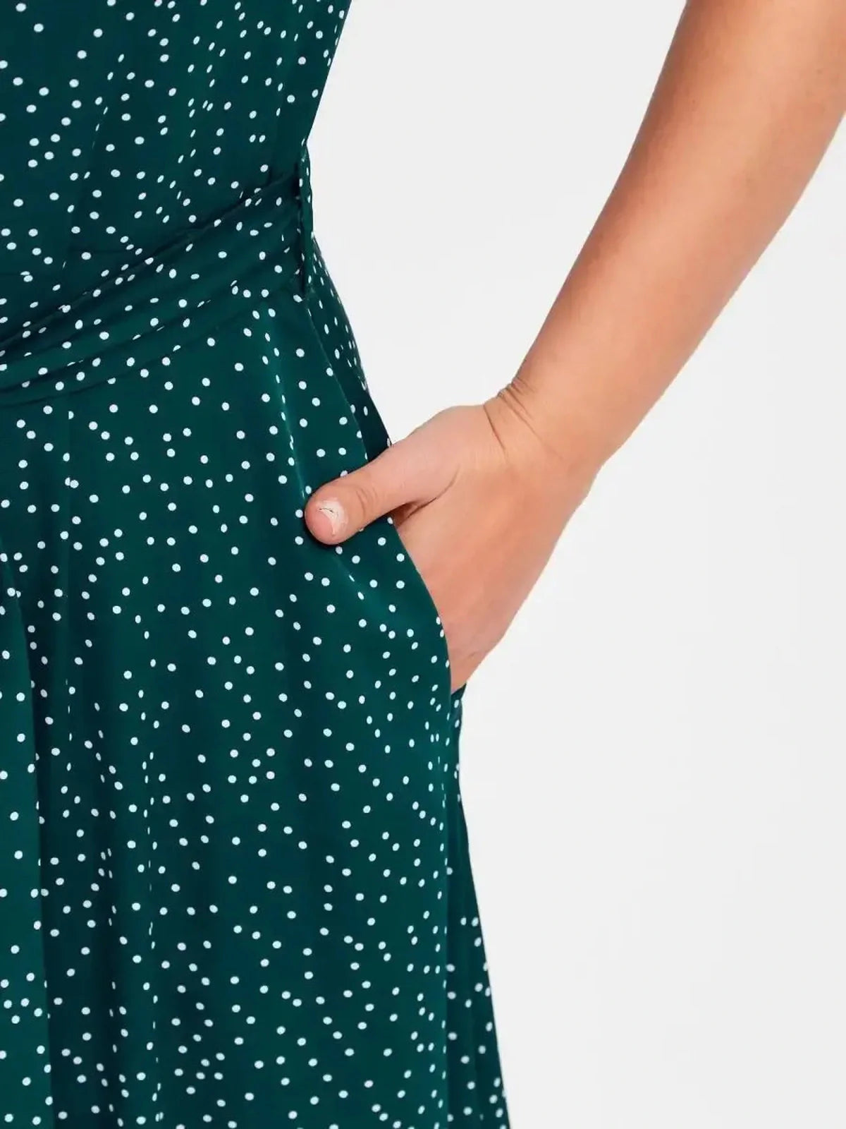 Close-up of a woman's hand in the pocket of an emerald green dot midi dress with white polka dots.