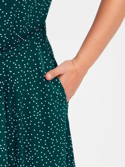 Close-up of a woman's hand in the pocket of an emerald green dot midi dress with white polka dots.