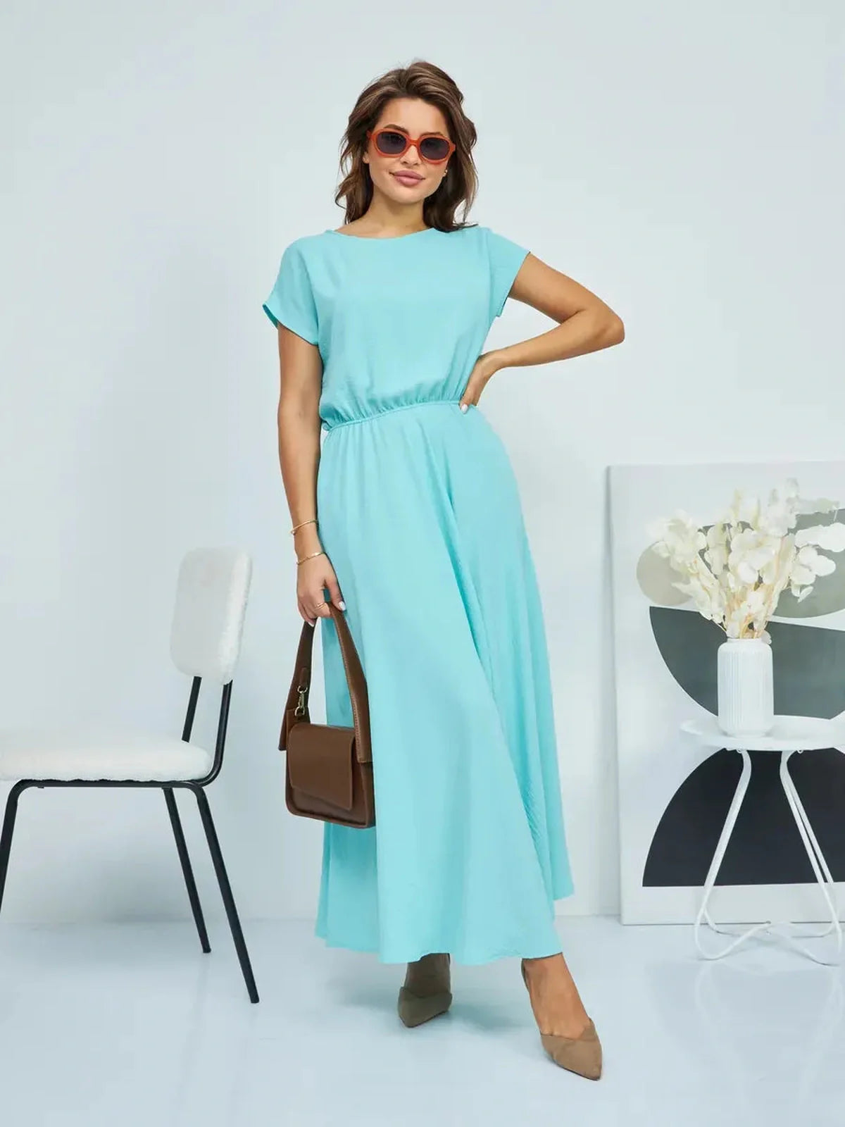 Woman wearing a light blue maxi dress with a cinched waist, accessorized with sunglasses, perfect for summer outings.