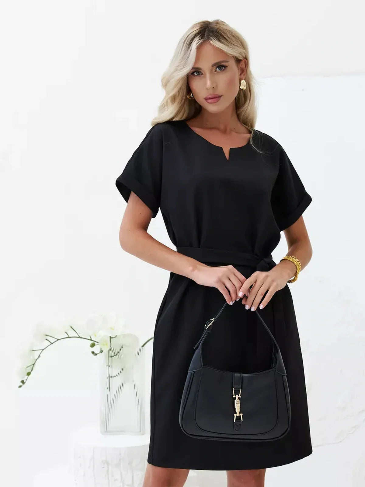 Confidently elegant woman in a black Modern Grace mini dress with a self-tie belt and a stylish handbag.