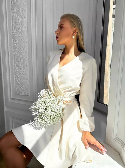 Ivory Whisper mini dress featuring a wrap-effect bodice and long sleeves, styled with delicate flowers.
