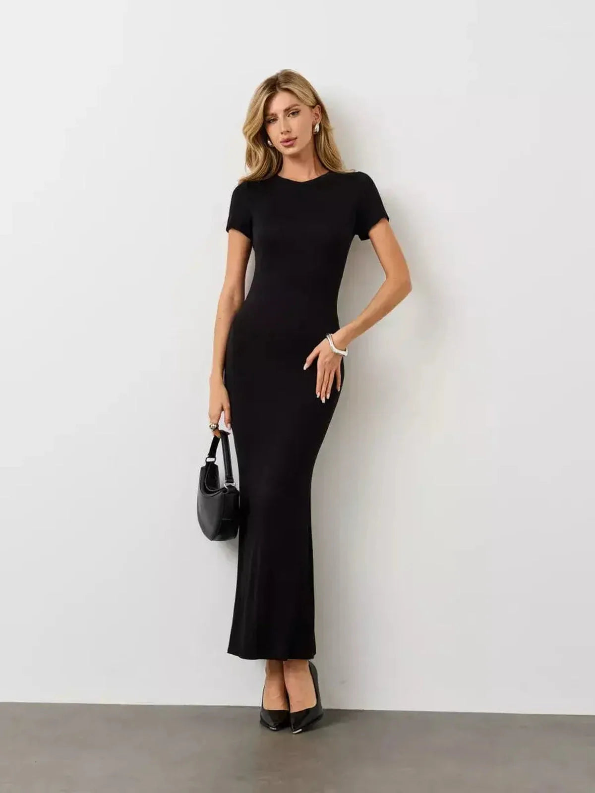 Model wearing a Noir Curve Maxi Dress in iconic black, featuring a sculpted silhouette and flared hem.