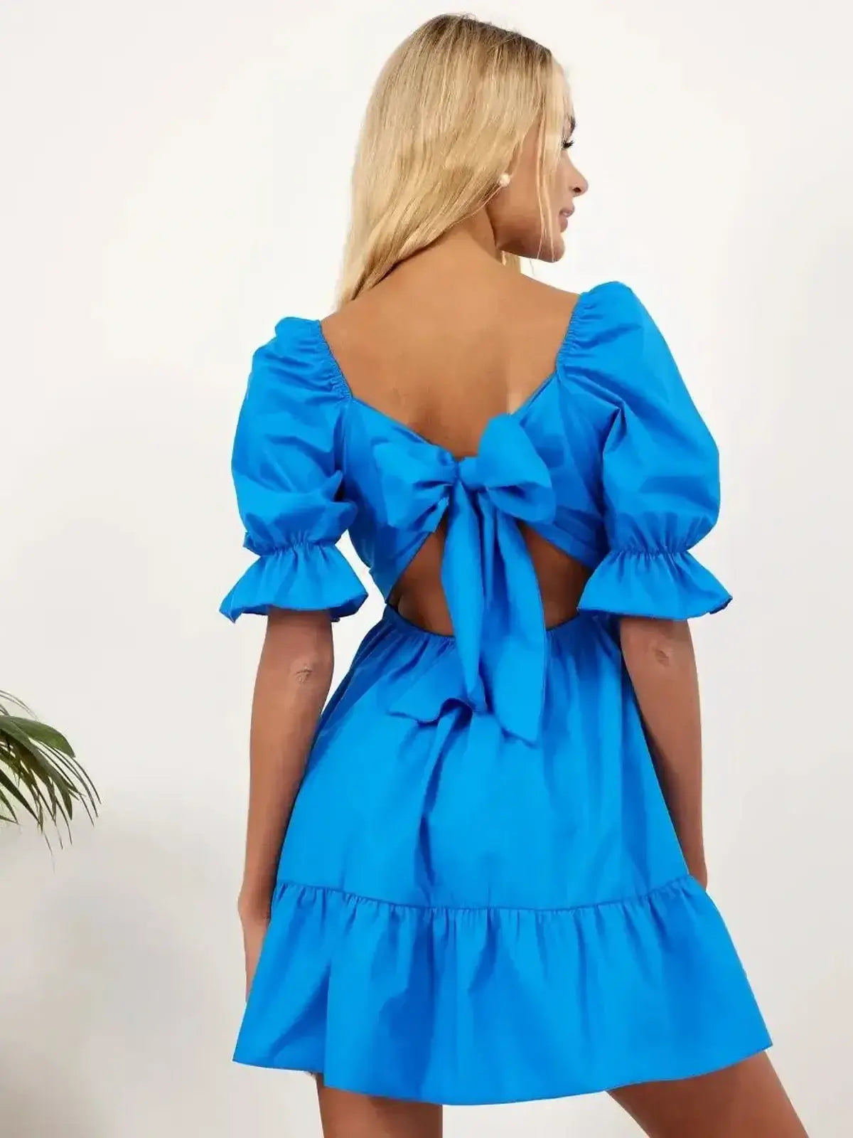Model showcasing the Electric Charm blue mini dress with open back and dramatic bow tie, ideal for summer and special occasions.