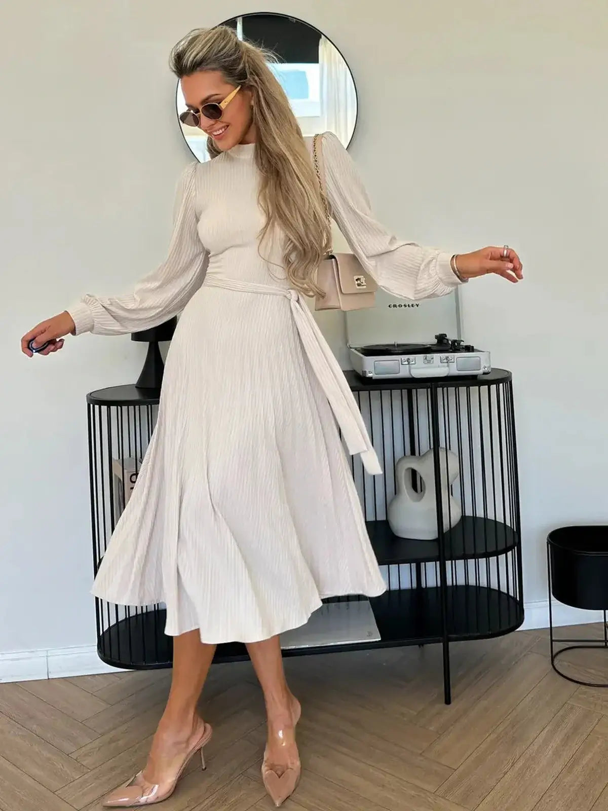 Model showcasing the Ivory Whisper Midi Dress with flowing pleated skirt and high neck in an elegant setting.