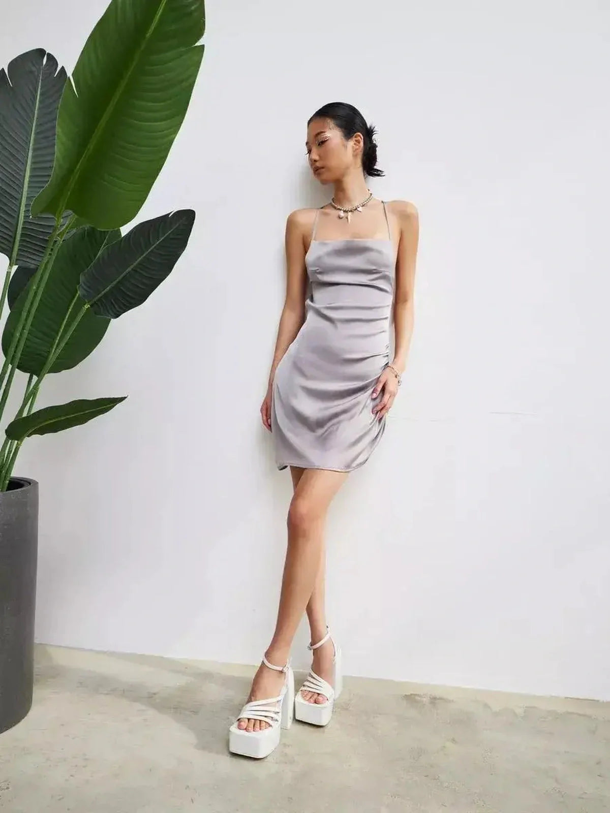 Model showcasing the Silken Rush mini dress in silver-gray, highlighting its sleek design and backless silhouette.