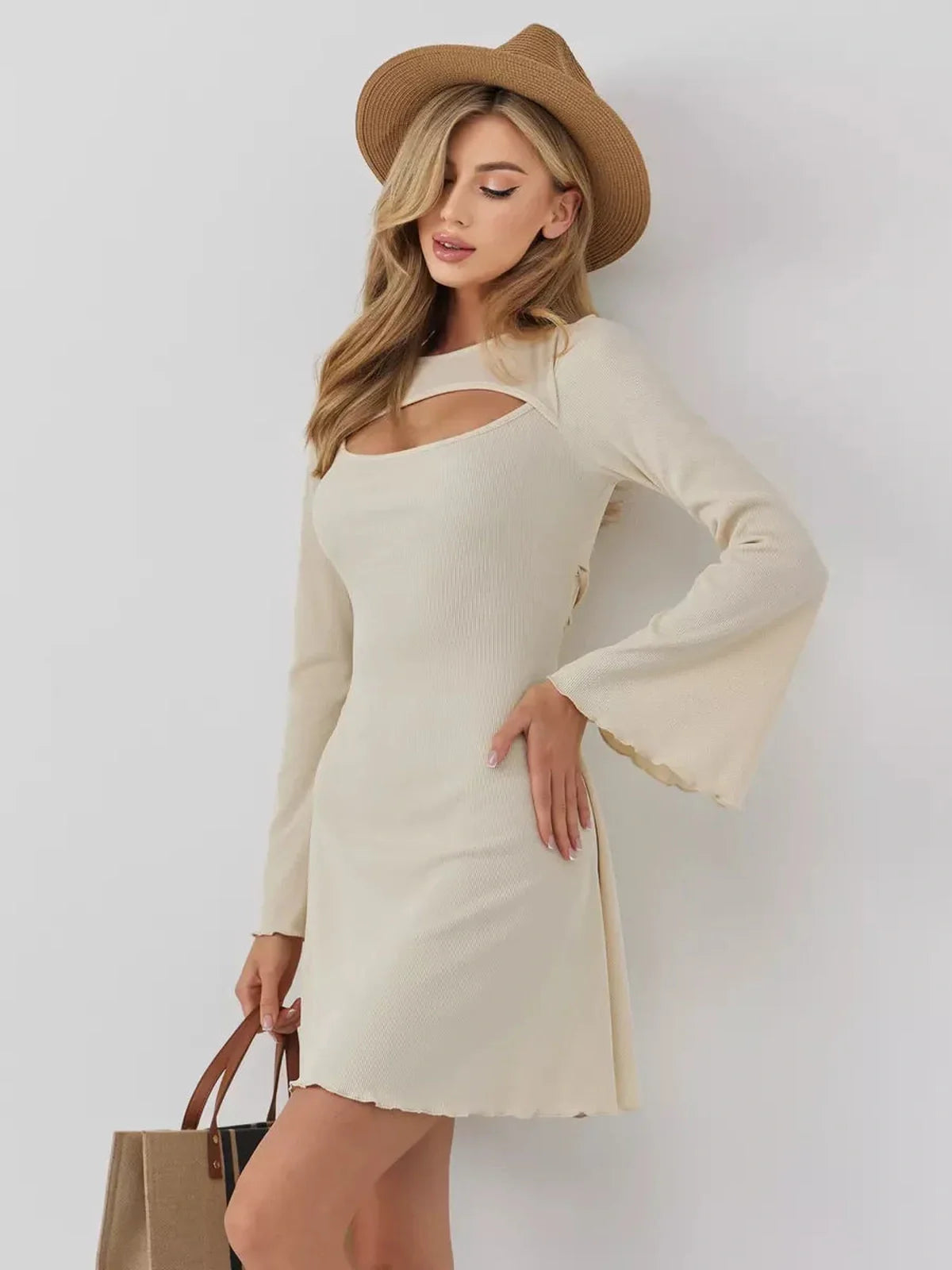 Model wearing the Sculpted Grace mini dress in cream with long sleeves and a front cutout, styled with a hat.