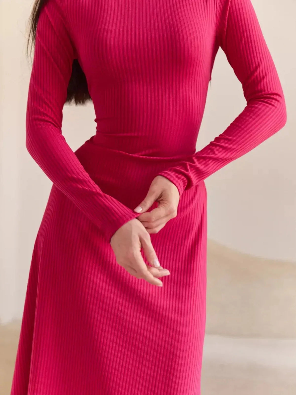 Close-up of a woman adjusting the sleeves of a pink contour midi dress, showcasing its ribbed knit texture and elegant fit.