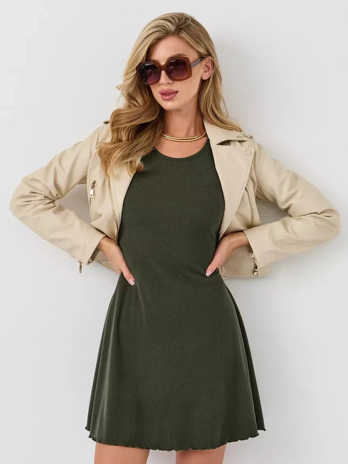 Model wearing an olive mini dress with a beige jacket and sunglasses, showcasing a chic summer outfit.
