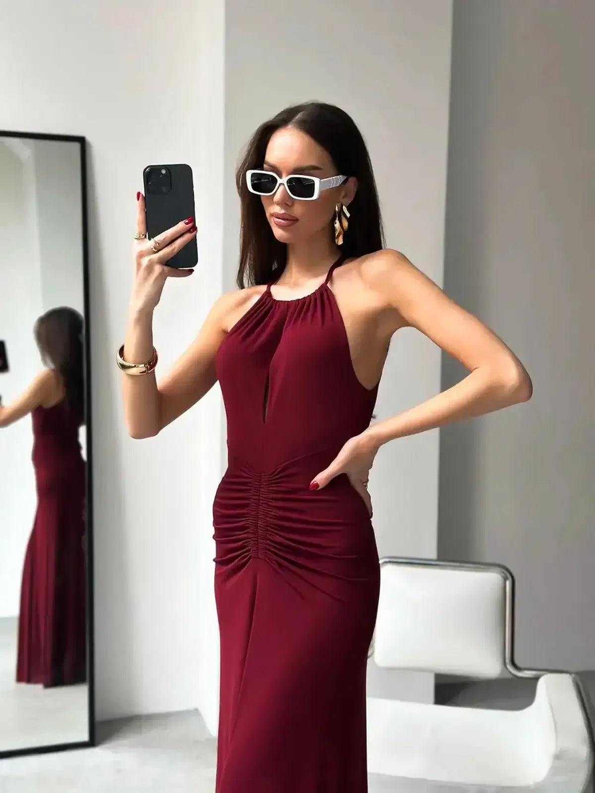 Model showcasing a burgundy maxi dress with a halter neckline and ruched waist, perfect for formal occasions.