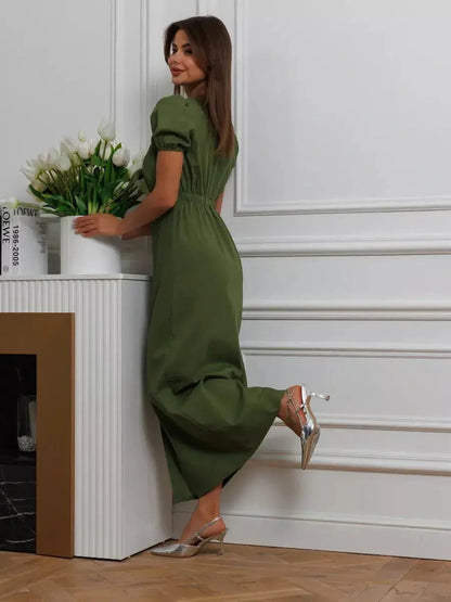 Woman in an olive green maxi dress with puff sleeves, styled elegantly in a chic indoor setting.
