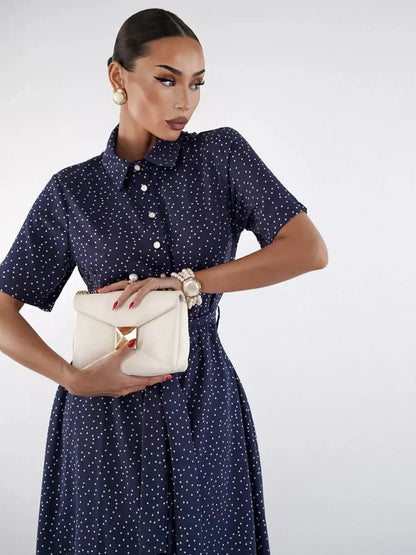 Model wearing a Midnight Dot Midi Dress in navy with white dots, holding a chic clutch for an elegant outfit look.