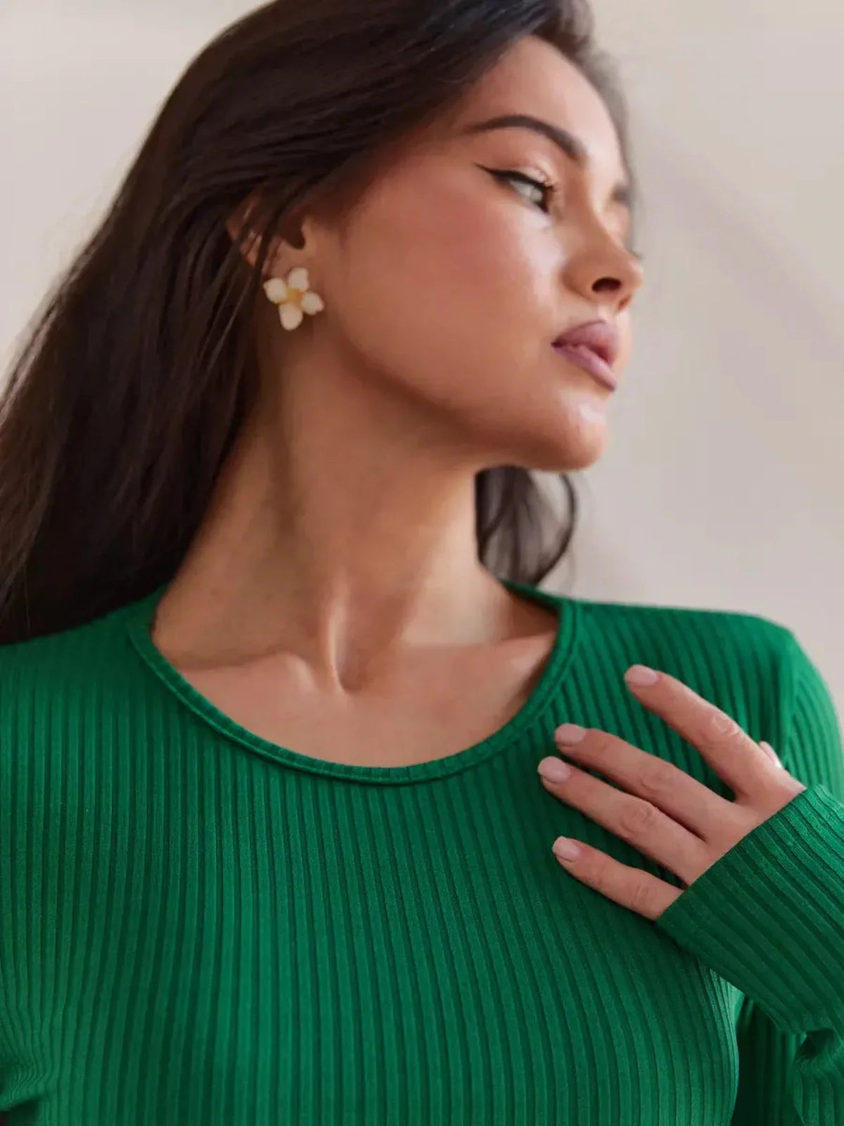 Close-up of a woman in a ribbed green top showcasing elegant earrings and soft makeup.