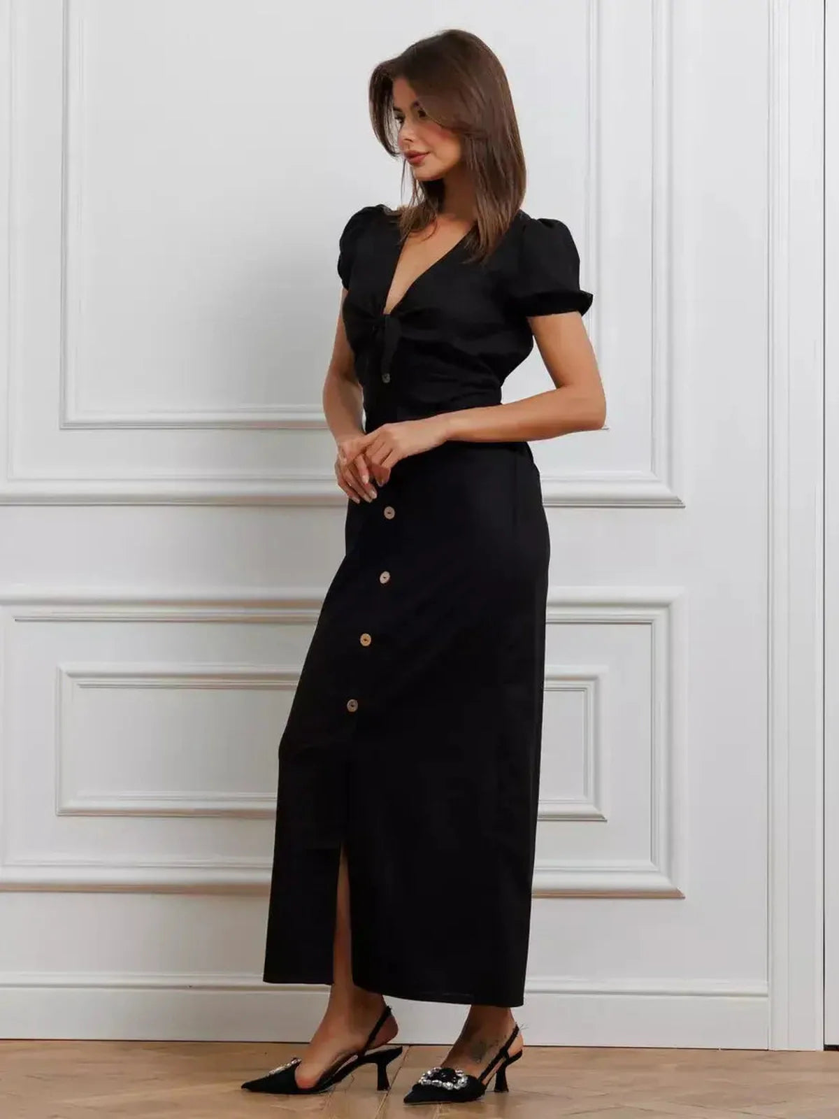 Elegant black maxi dress with tie-front detail, puff sleeves, and contrast buttons, perfect for weddings and formal events.