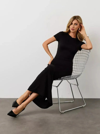 Woman in a black maxi dress with a sculpted silhouette sitting on a modern chair, showcasing minimalist style.