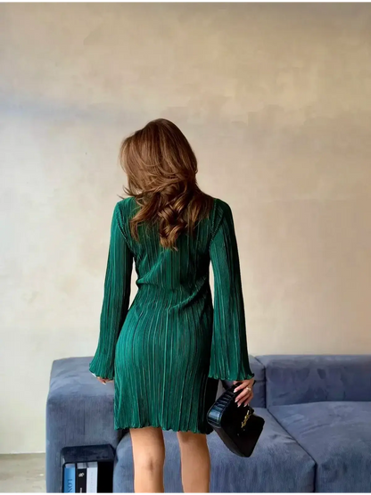 Back view of a woman in an emerald green mini dress with bell sleeves, showcasing its pleated texture and elegant silhouette.