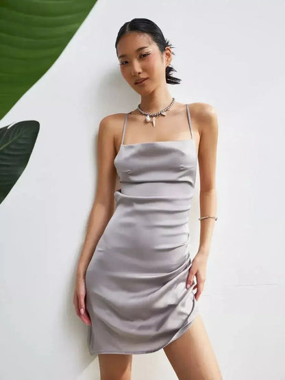A model wearing a slim-fit, satin-effect mini dress in silver-gray, showcasing summer elegance and sultry ruching.