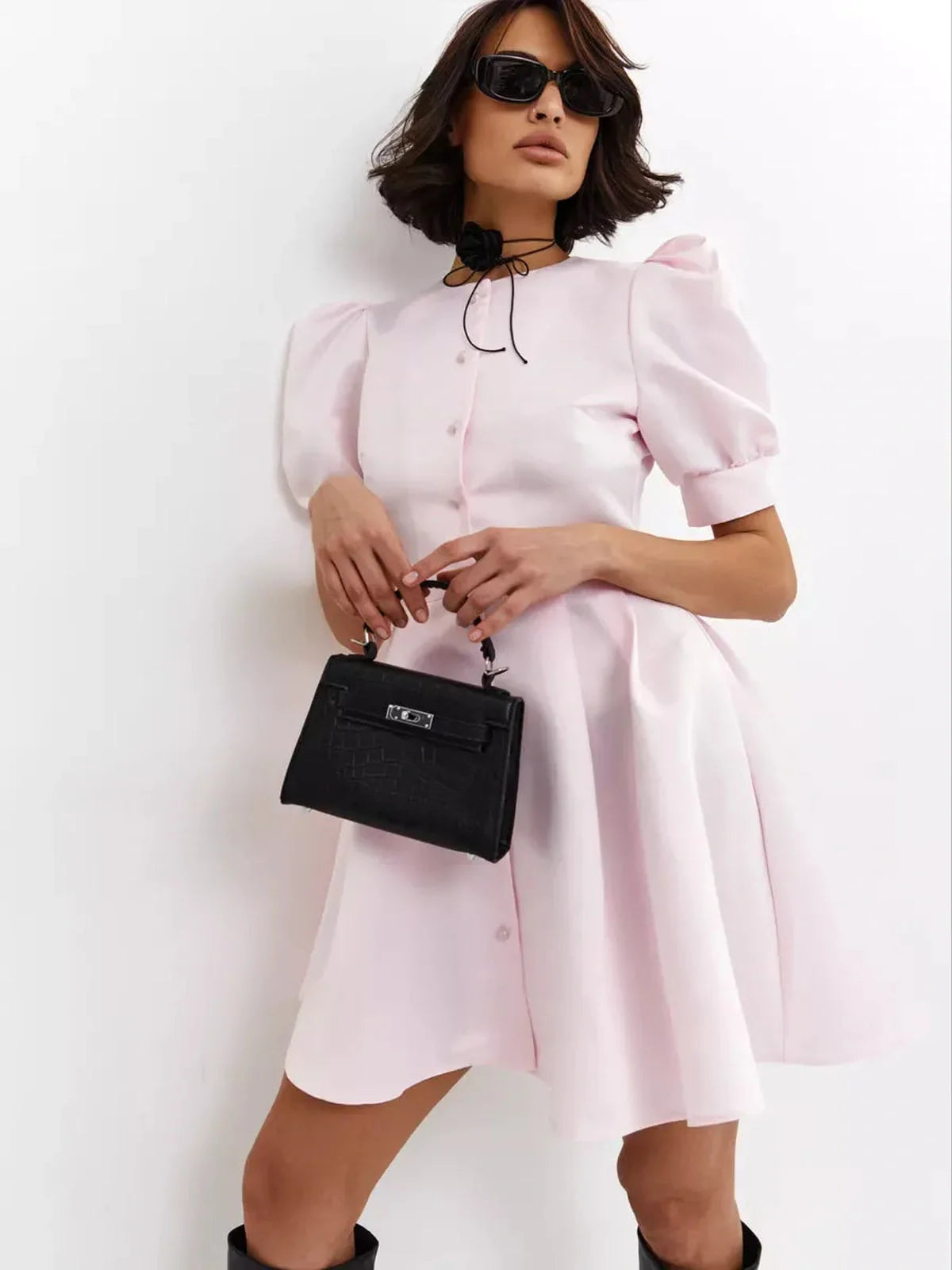 Model wearing a Pearl Puff Mini Dress in pink with puff sleeves and a stylish handbag, perfect for summer events.