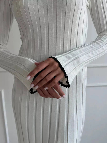 Close-up of a woman's hands in a ribbed ivory maxi dress, showcasing elegant long sleeves with delicate black ruffle trim.