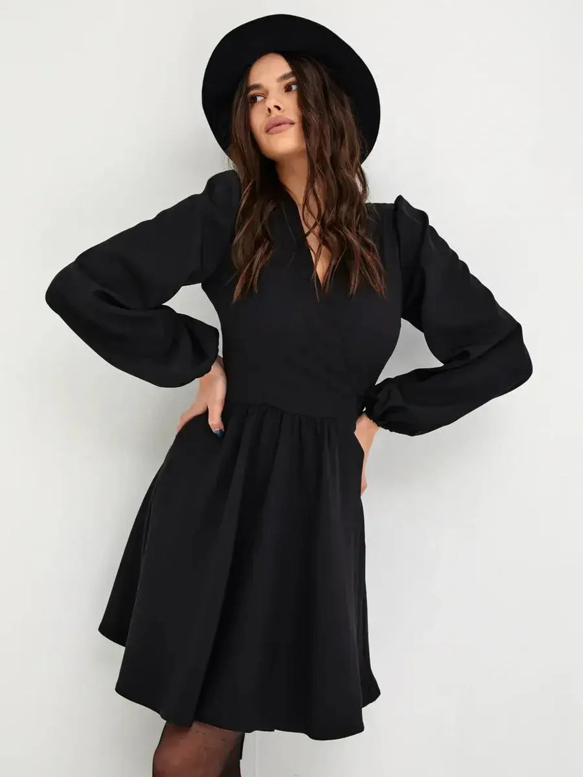 Stylish woman wearing a black mini dress with long sleeves and a V-neckline, paired with a chic hat.