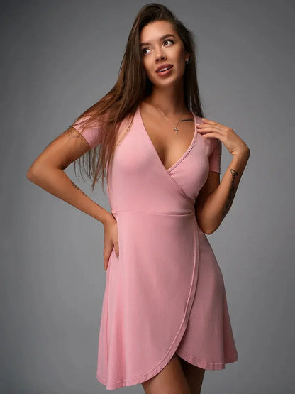 Woman wearing a flattering blush pink wrap-style mini dress with a deep V-neckline and tulip hemline.