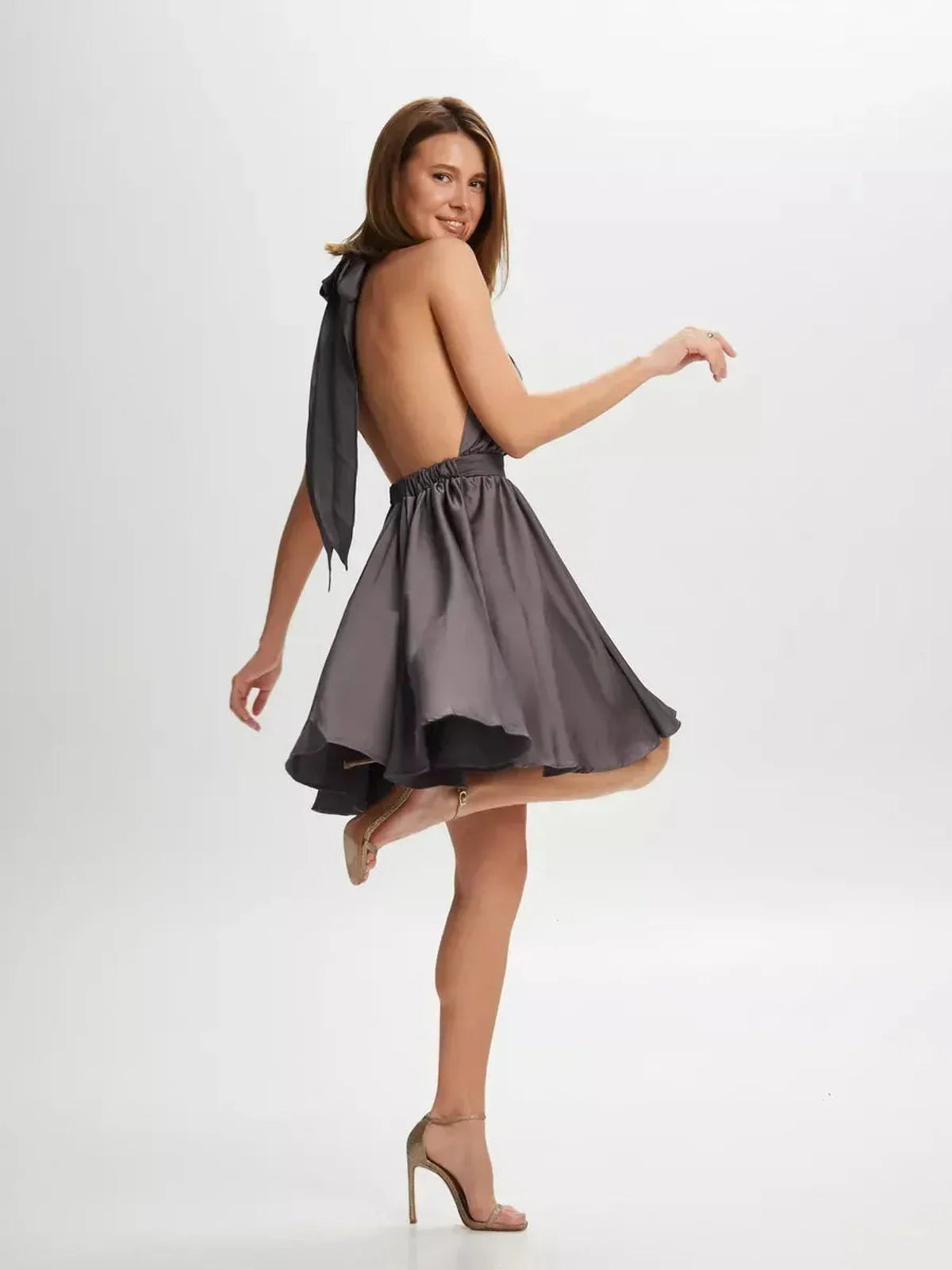 Model showcasing the Satin Whisper mini dress, featuring a plunging back and elegant halter tie, perfect for weddings and parties.